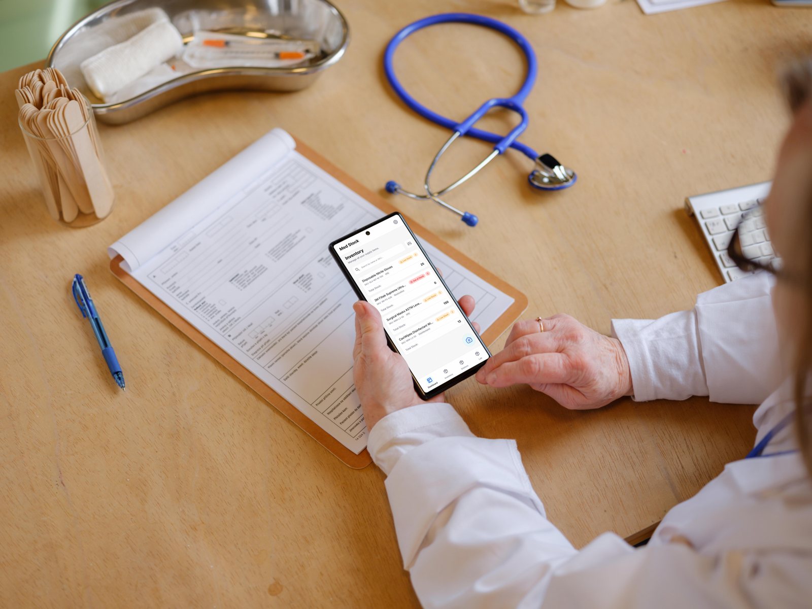 A medical professional in a clinical setting holding a smartphone, actively using the MedStock native app to manage inventory levels alongside traditional medical tools.